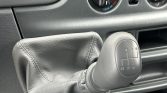 Close-up of a manual gear shift knob with a 5-speed pattern and boot, dashboard vents in the background.
