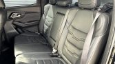 Back seat area of a dark leather SUV with three seats and headrests, seat belts visible on the ends and middle seatbelt buckles showing at the sides.