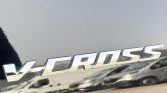 Chrome V-CROSS badge on a dark car panel, reflecting the surroundings in the letters.