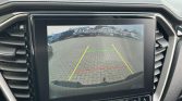 Car rearview camera display showing parking guide lines (green, yellow, red) on a brick parking lot; text reads 'Check surroundings for safety'.