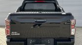 Rear view of a black Isuzu D-Max pickup with a roll bar and bed cover, parked on a brick-paved surface