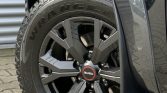Close-up of a dark gray Isuzu SUV wheel with a black alloy rim and a Goodyear Wrangler tire visible at the fender.