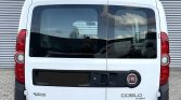 White Fiat Doblo max van rear view with roof rack and hitch, parked on a paved lot.