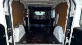 Empty white cargo van interior, plywood side panels, black rubber floor, wheel wells, rear doors open.