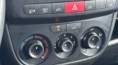 Car climate control panel: left temperature dial from blue to red, middle fan speed dial labeled 0–4, right airflow/defrost dial with feet and windshield icons; hazard light button (red triangle) above and a recirculation button nearby; small illuminated indicator on a separate control.