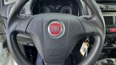 Steering wheel with Fiat emblem in a car interior; dashboard gauges in the background