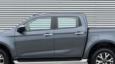 Side view of a gray double-cab pickup truck parked in front of a metal corrugated wall