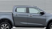 Gray pickup truck in profile view parked against a metal corrugated backdrop; four-door crew cab with alloy wheels.