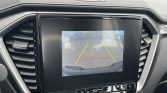 In-car rearview camera display with green, yellow, and red parking guidelines and 'Check surroundings for safety' text.