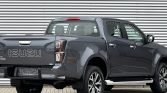 Rear-left three-quarter view of a grey Isuzu D-Max pickup truck parked beside a corrugated metal wall.