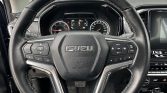 Close-up of a black leather steering wheel with chrome accents and the ISUZU logo, showing built-in controls in a car interior.