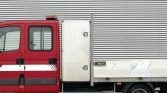 Red flatbed tow truck with a white horizontal stripe parked in front of a corrugated metal wall.