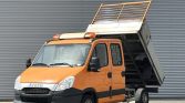 Orange Iveco dump truck with its bed raised, ready to unload, parked in front of a corrugated metal wall.