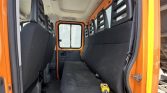 Interior of an orange utility van showing a long black bench seat and two front seats, with a yellow handheld multimeter resting on the seat.