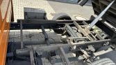 Under carriage of a heavy truck: exposed frame, leaf springs, and a hydraulic shock absorber visible under the chassis without wheels on one side.