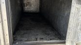 Open metal storage compartment on a utility vehicle, empty and dusty, with a small door at the far end inside the box.