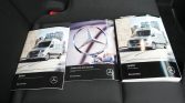 Three Mercedes-Benz brochures spread on a dark car seat, featuring a Sprinter van and the Mercedes logo central to the layout.