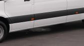 Side view of a white van with a black lower side panel, orange side marker lights, and a closed sliding door on a dark pavement surface.