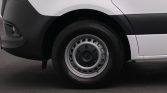 Front wheel and tire of a white van, showing the steel rim and black bumper area