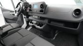 Front cabin of a van showing steering wheel, dashboard, touchscreen infotainment, and cup holders on the center console.