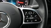 Close-up of a Mercedes steering wheel showing a glossy control panel with volume wheel, phone, voice/mute icons, and star button.