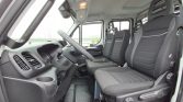 Interior of a van cab with a three-seat front row, black fabric seats, and a steering wheel on the left side ready for driving