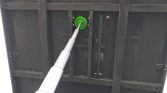 Green circular valve on a dark metal panel with a silver telescoping pipe entering it.