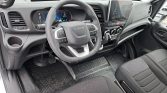 Interior view of a modern Iveco van dashboard with steering wheel, digital gauge cluster, center touchscreen, gear shifter, and black fabric seats.
