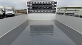 Flatbed truck bed with tall decorative guardrail featuring rows of circular holes, reflecting on the shiny floor in a parking lot setting