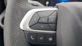 Close-up of a car steering wheel control pad: four-directional arrows surrounding an 'OK' button; below are three buttons for phone, voice, and a documents/menu icon.