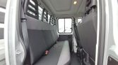 Interior of a white van showing a long rear bench seat and side door with black upholstery in a cargo van interior.