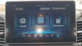Infotainment home screen with three feature tiles: Driving Style, Assistance Non Stop, and Remote Assistance, plus Settings and Vehicle Information at the top and control icons along the bottom edge of the screen.