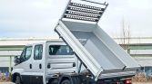 Silver cab truck with a raised dump bed, ready to unload cargo on a paved lot.