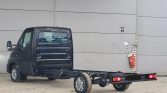 Black delivery van with a long chassis frame extending from the rear, no cargo bed installed, parked outdoors against a gray wall.