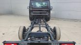 Rear view of a black Iveco Daily truck chassis with exposed steel frame and dual rear wheels, against a gray wall.