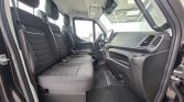 Interior of a left-hand-drive van with three front seats in black fabric, seat belts fastened, and a dashboard with a left-side steering wheel.
