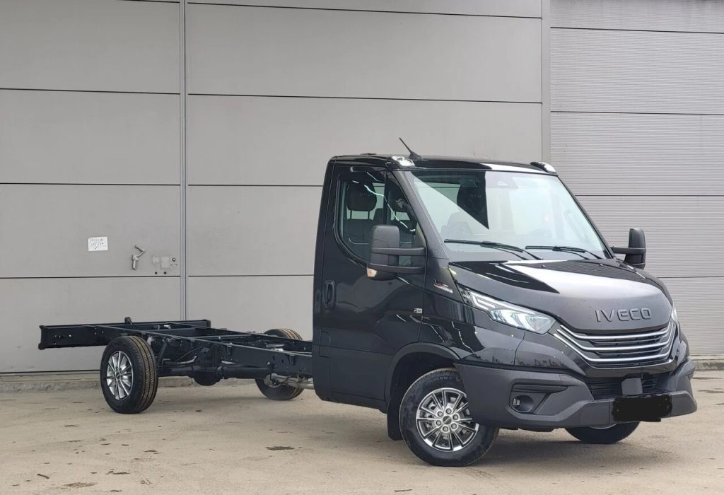Black Iveco cab-over truck with exposed chassis, parked outdoors in front of a gray industrial wall.