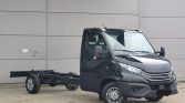 Black Iveco cab-over truck with exposed chassis, parked outdoors in front of a gray industrial wall.