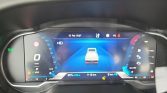 Digital car dashboard showing a rear view of a white pickup on a blue tunnel, center display for driver with speed 0 km/h left, right needle gauge, eco indicator below left, warning icons bottom center