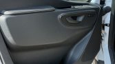 Car door interior panel with a padded armrest, window controls, and a speaker grille visible on the lower door surface
