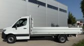 White flatbed truck parked beside a gray industrial building in a loading area