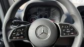 Close-up of a Mercedes-Benz steering wheel with cruise control and media buttons, dashboard visible behind it