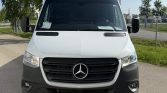 Front view of a white Mercedes-Benz van with a black grille parked outdoors, showing the emblem and headlights facing the camera on a sunny day