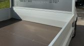Open flatbed of a white utility truck with a brown non-slip bed surface and metal side rails.
