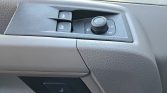 Car door interior panel with power window switches, mirror adjust knob, and lock buttons on textured black trim.