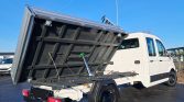 White dump truck with its cargo bed raised at an angle, hydraulic piston visible in the bed's underside.