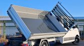 White dump truck with its cargo bed tilted upward, as if unloading material, parked on a paved surface under a blue sky.