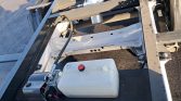 White plastic reservoir with red cap attached to a hydraulic pump on a metal chassis, with hoses and wiring nearby.