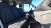 Interior of a white van: driver and front passenger seats, steering wheel, and dashboard visible against a blue sky outside.