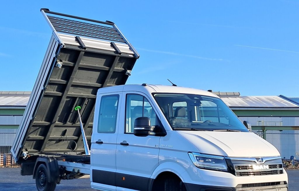 White cab-forward truck with its dump bed raised, ready to unload under a clear blue sky.